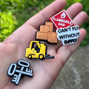 Może przedstawiać: Zestaw pięciu kolorowych zawieszek do butów, w tym wózek widłowy, pudełka, klucz i czerwony znak z napisem "Flammable Gas" oraz biały znak z napisem "Can't Fly Without Supply".