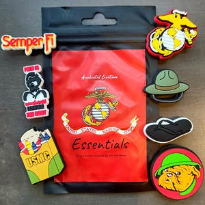 May include: A selection of shoe charms with a United States Marine Corps theme. The charms feature the Marine Corps emblem, a bulldog, a drill instructor's hat, and the words "Semper Fi" and "USMC". The charms are in various colours.