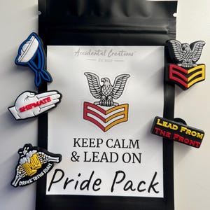 May include: A black zippered pouch with a white background containing a variety of colorful shoe charms. The charms feature images of a beer mug, a shipmate hand gesture, a bald eagle, and a military rank insignia. The text "Keep Calm & Lead On" and "Pride Pack" are printed on the pouch.
