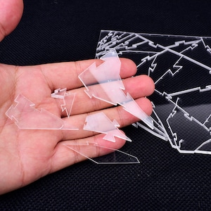 May include: Clear acrylic puzzle pieces in the shape of lightning bolts are held in a hand. A larger, assembled puzzle is visible in the background. The pieces are transparent and have a geometric design.