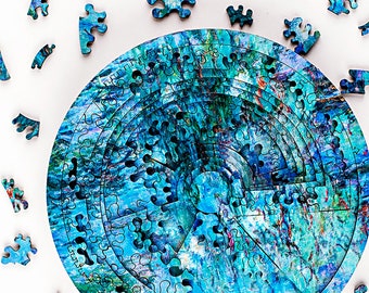 Op de afbeelding: Een gedeeltelijk geassembleerde cirkelvormige legpuzzel met een blauw en groen abstract ontwerp. Verschillende puzzelstukjes liggen verspreid op een witte achtergrond. Het ontwerp van de puzzel bevat wervelingen en patronen.