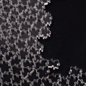 Puede incluir: Piezas de rompecabezas de acr&iacute;lico transparente con un dise&ntilde;o hexagonal &uacute;nico. Las piezas se entrelazan para formar una forma m&aacute;s grande, con algunas piezas separadas. El fondo es negro s&oacute;lido, creando un contraste con el rompecabezas transparente.