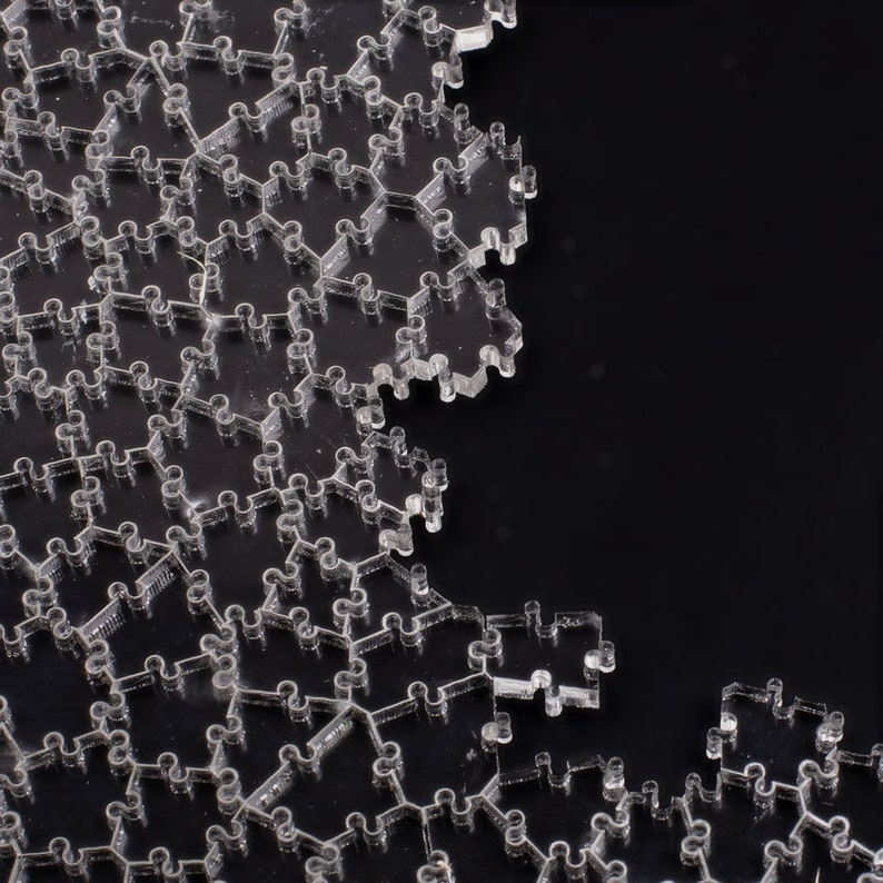 Puede incluir: Piezas de rompecabezas de acr&iacute;lico transparente con un dise&ntilde;o hexagonal &uacute;nico. Las piezas se entrelazan para formar una forma m&aacute;s grande, con algunas piezas separadas. El fondo es negro s&oacute;lido, creando un contraste con el rompecabezas transparente.