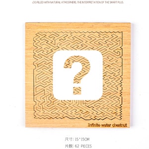 Puede incluir: Un rompecabezas cuadrado de madera con un dise&ntilde;o de laberinto y un gran signo de interrogaci&oacute;n recortado en el centro. El rompecabezas mide 15 cm x 15 cm y contiene 62 piezas. El texto "Infinite water chestnut" est&aacute; impreso en la parte inferior.