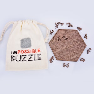 May include: A wooden hexagonal puzzle with intricate patterns, partially assembled, surrounded by loose pieces. A canvas bag with the words "IMPOSSIBLE PUZZLE" printed on it is on the left. The puzzle is a challenging brain teaser.