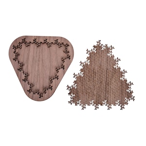 Puede incluir: Dos rompecabezas de madera. Uno es de forma triangular marrón oscuro con un patrón geométrico complejo. El otro es un rompecabezas de madera en forma de corazón con un borde decorativo de pequeñas formas intrincadas. Ambos rompecabezas están sobre un fondo blanco.