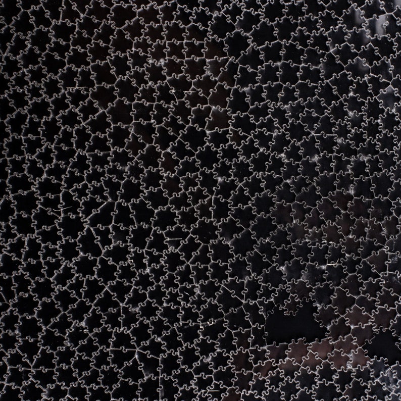 Puede incluir: Primer plano de una superficie negra cubierta por un patr&oacute;n de piezas de rompecabezas entrelazadas. Las piezas est&aacute;n delineadas en un color claro, creando un contraste. El efecto general es un dise&ntilde;o geom&eacute;trico texturizado.