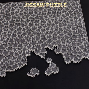 Puede incluir: Un rompecabezas de acr&iacute;lico transparente con piezas entrelazadas, parcialmente ensamblado. Las palabras "JIGSAW PUZZLE" est&aacute;n impresas en la parte superior. Varias piezas est&aacute;n separadas, mostrando el dise&ntilde;o del rompecabezas.