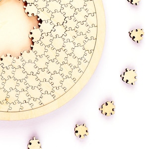 Könnte beinhalten: Ein teilweise zusammengesetztes Holzpuzzle mit kreisförmigem Design. Die hellbraunen Puzzleteile sind am Rand verstreut. Der Hintergrund ist weiß.