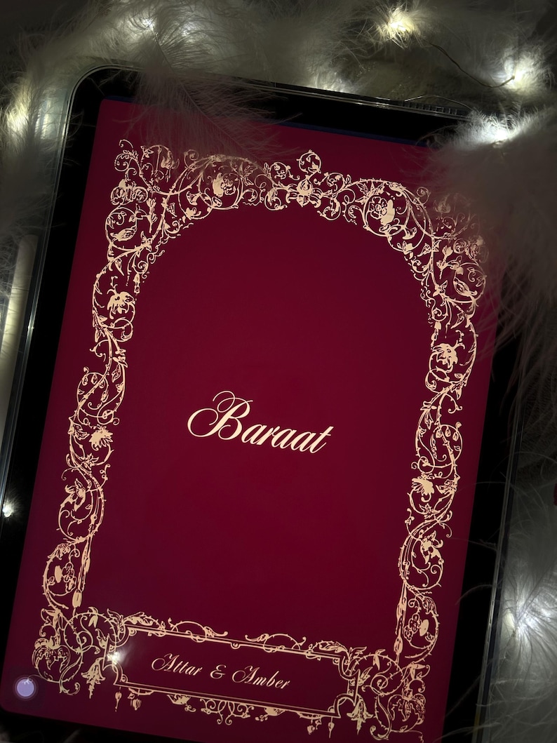 Puede incluir: Una pantalla de tableta de color burdeos muestra la palabra "Baraat" en una elegante escritura, enmarcada por dise&ntilde;os florales dorados. El texto "Attar & Amber" est&aacute; debajo. La imagen est&aacute; rodeada de suaves plumas blancas y luces de hadas.