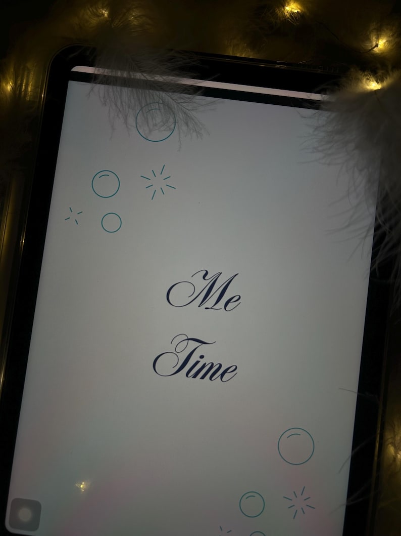 Puede incluir: Una tableta digital muestra las palabras "Me Time" en una elegante escritura. La pantalla es blanca con c&iacute;rculos y estrellas azules decorativas. La tableta est&aacute; rodeada de suaves plumas blancas y luces doradas c&aacute;lidas.