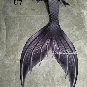 Könnte beinhalten: Ein schwarzer Meerjungfrauen-Schwanz mit einem dunkelgrauen und weißen Muster. Der Schwanz hat eine Flosse mit einer spitzen Spitze und einer strukturierten Oberfläche.