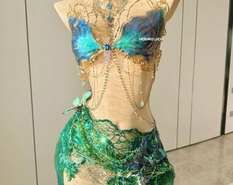 May include: A mermaid-themed costume displayed on a mannequin. The top is blue and green with gold accents and a jeweled necklace. The bottom is a green skirt with lace and sequin details. The text "MERMAID LUCIA" is visible.
