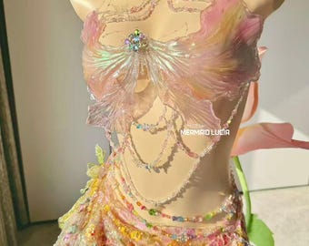 May include: A fantasy-themed outfit with a floral design. The top features iridescent, petal-like shapes and a central jewel. The skirt is adorned with colorful floral embellishments and beads. The text "MERMAID LUCIA" is visible.