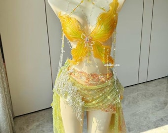 May include: A yellow and green butterfly-themed costume displayed on a mannequin. The costume features a bodice with large butterfly wing designs, a beaded necklace, and a skirt with lace and beaded accents. The costume is designed with a fairy or fantasy theme.