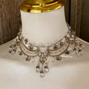 Könnte beinhalten: Eine mehrlagige goldfarbene Halskette mit Kristallperlen und Schmetterlingsanhängern. Die Halskette hat ein zartes, feminines Design und verfügt über einen baumelnden Kristallanhänger.