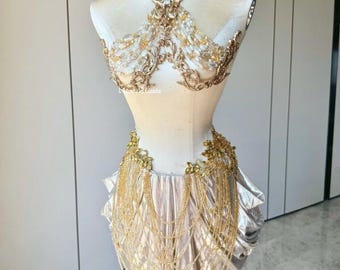 Puede incluir: Conjunto de corpiño y falda dorados y ornamentados, expuesto sobre un maniquí. El corpiño presenta intrincados detalles de filigrana y cristal, mientras que la falda es un diseño drapeado y brillante. El conjunto incluye un collar gargantilla a juego y detalles de cuentas en cascada.
