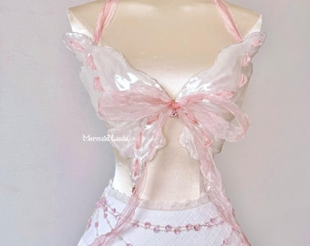 May include: A pink and white butterfly-shaped top with a white skirt and pink beaded embellishments. The top is made of sheer fabric and has a halter neckline.