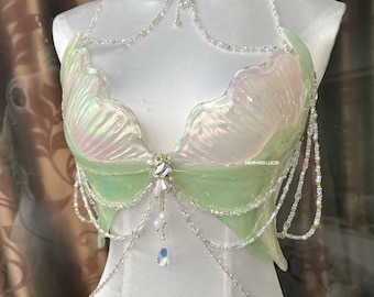 May include: A mermaid-themed top and choker set. The top is a light green and iridescent material, with a scalloped edge and beaded accents. The choker is a matching design with a central jewel and dangling beads. The set is displayed on a white mannequin.