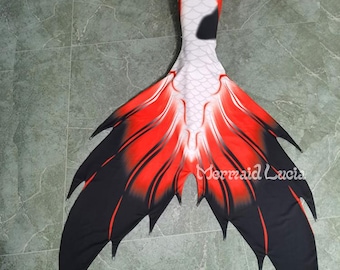 May include: A mermaid tail with a koi fish design. The tail features a white body with red and black accents, and a large, fan-shaped tail fin. The text "Mermaid Lucia" is visible on the tail.