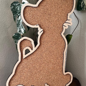 May include: A wooden corkboard shaped like a cartoon lion with the name "David" engraved on the bottom. The corkboard is brown and has a natural wood finish.