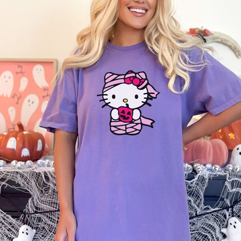 May include: Purple t-shirt featuring a graphic of Hello Kitty dressed as a mummy holding a pumpkin.