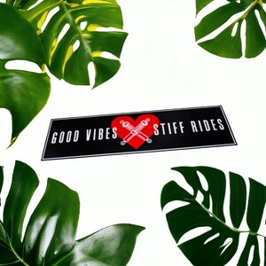 May include: Black and white sticker with a red heart and the text "GOOD VIBES STIFF RIDES". The sticker is surrounded by green tropical leaves.
