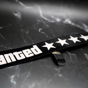May include: A black and white "Wanted" sign with five white stars. The sign is connected to a black connector with multiple pins.
