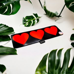 May include: Three red hearts on a black background. The hearts are arranged in a row, with the largest heart in the center.