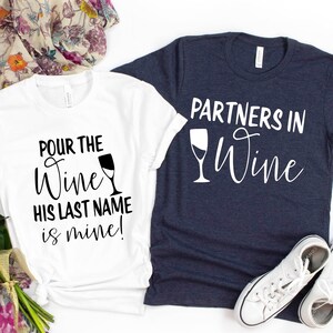 May include: Two white t-shirts with black text and a wine glass graphic. The first shirt says "Pour the Wine His Last Name is Mine!" The second shirt says "Partners in Wine".