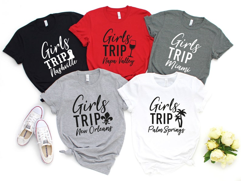 以下が含まれることがあります： 「Girls Trip」の文字と各目的地がプリントされたTシャツが5枚。目的地はナッシュビル、ナパバレー、マイアミ、ニューオーリンズ、パームスプリングスです。