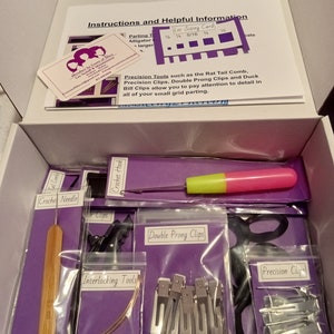 Puede incluir: Una caja morada llena de herramientas para peinar el cabello, que incluyen un gancho de ganchillo, una aguja de ganchillo, un peine de cola de rata, pinzas de doble punta, pinzas de precisión y herramientas entrelazadas. La caja también incluye una tarjeta con instrucciones e información útil.