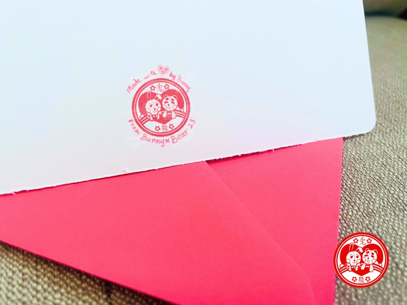 Puede incluir: Un sello rojo y blanco con un coraz&oacute;n y dos animales de dibujos animados. El sello dice "Made with love by Bunnies from Bunny x Bear 23".