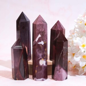 Puede incluir: Cinco puntas de cristal pulidas, con rayas de color púrpura oscuro y blanco, dispuestas sobre una base de madera. Las puntas son de diferentes tamaños y formas, y tienen un aspecto natural y orgánico.