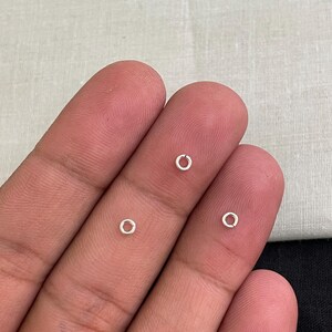 Op de afbeelding: Close-up van drie kleine, zilverkleurige verbindingsringen. Deze open ringen worden gebruikt bij het maken van sieraden om onderdelen te verbinden. De ringen worden getoond tegen een neutrale achtergrond, wat hun eenvoudige, cirkelvormige ontwerp benadrukt.
