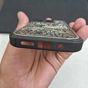 May include: A black phone case with a silver, intricate, floral design. The case has cutouts for the phone's camera and speaker.