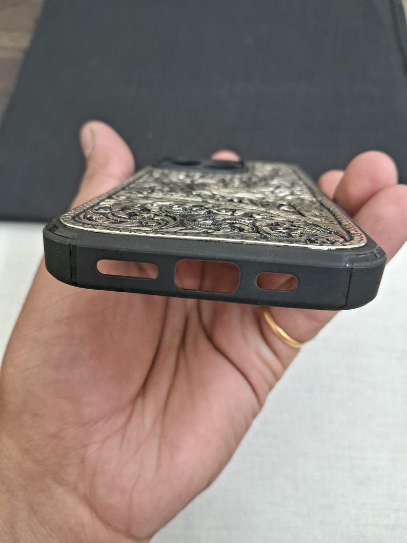 May include: A black phone case with a silver, intricate, floral design. The case has cutouts for the phone's camera and speaker.
