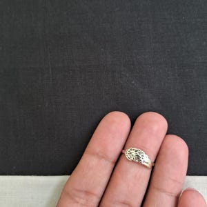 May include: A silver ring with a textured design. The ring is worn on a finger.