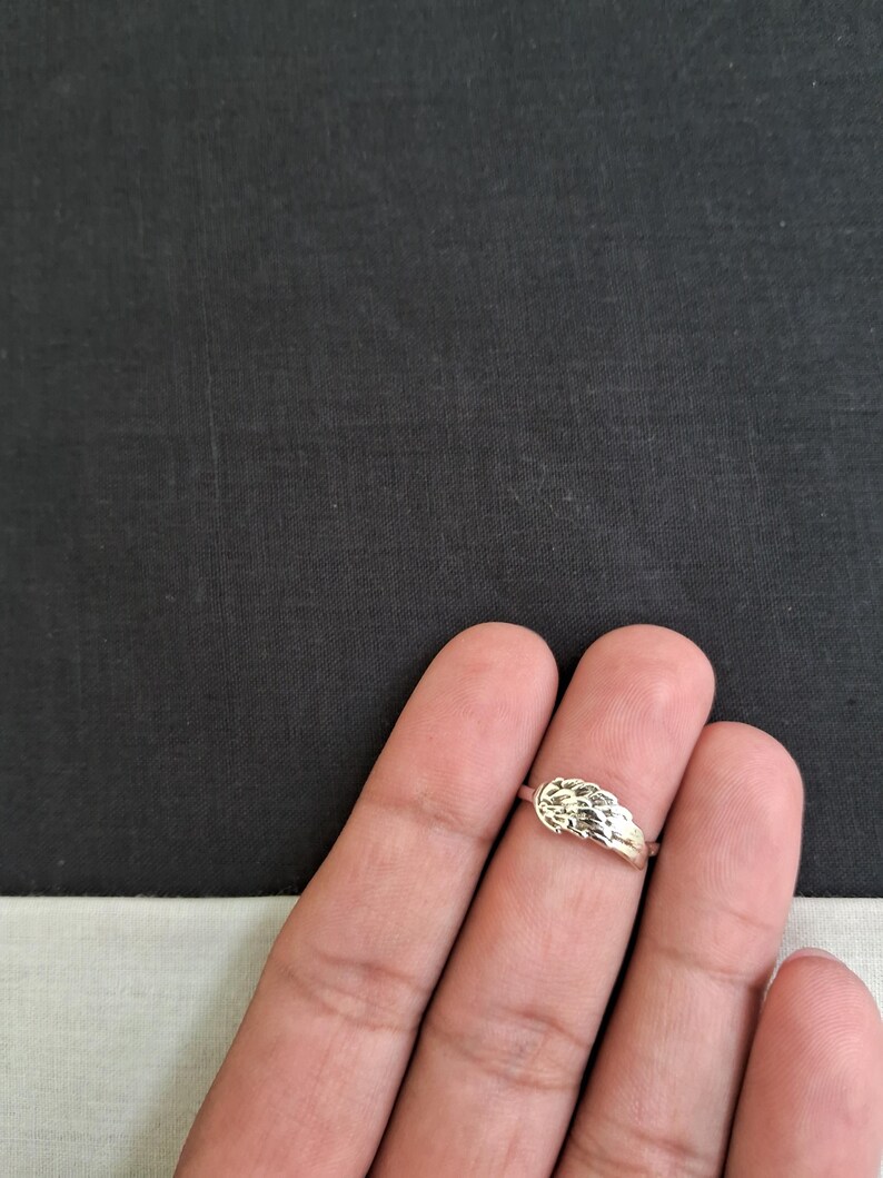 May include: A silver ring with a textured design. The ring is worn on a finger.
