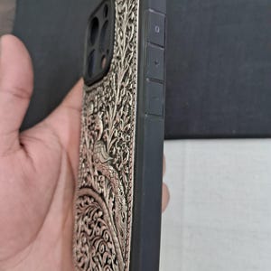 May include: A black phone case with a silver, intricate floral design. The case has a raised camera bump and volume buttons on the side.