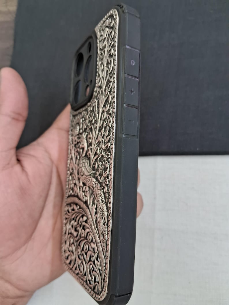 May include: A black phone case with a silver, intricate floral design. The case has a raised camera bump and volume buttons on the side.