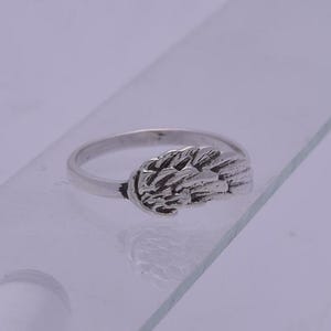May include: A silver ring with a wing design. The wing is detailed and textured.