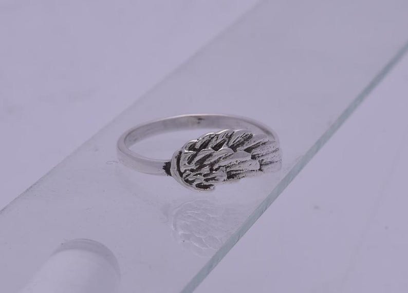 May include: A silver ring with a wing design. The wing is detailed and textured.