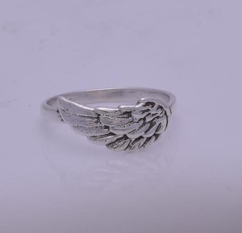 May include: A silver ring with an angel wing design. The wing is detailed and textured.