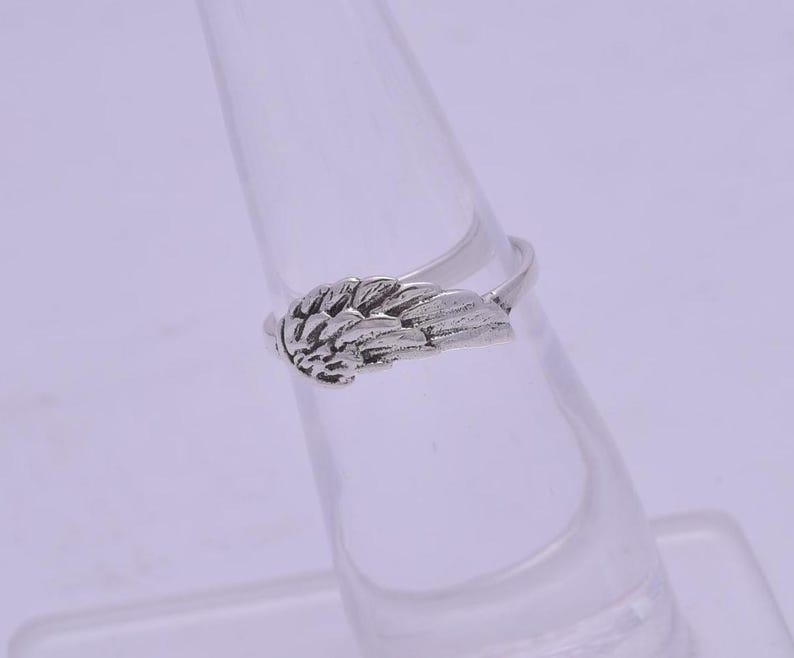 May include: A silver ring with a wing design. The wing is detailed and has a textured surface.