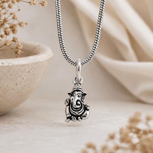Pu&ograve; includere: Una collana in metallo color argento con un piccolo ciondolo dettagliato della divinit&agrave; Ganesha. Il ciondolo &egrave; sospeso a una catena a serpente testurizzata, che mostra intagli complessi e una finitura ossidata che ne esalta i dettagli.