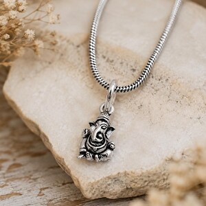 Pu&ograve; includere: Un ciondolo in metallo color argento a forma della divinit&agrave; Ganesha, caratterizzato da dettagli intricati e una postura seduta. Il ciondolo &egrave; sospeso a una catena a serpente color argento abbinata, con una finitura lucida e aree incavate scure.