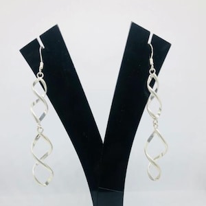 以下が含まれることがあります： ねじれた螺旋模様のシルバー製ドロップイヤリングのペア。イヤリングは黒いディスプレイスタンドに掛けられています。