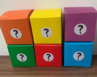Puede incluir: Seis cajas de colores con signos de interrogación. Las cajas están apiladas en dos filas de tres. Las cajas son naranja, amarilla, morada, verde, roja y azul.