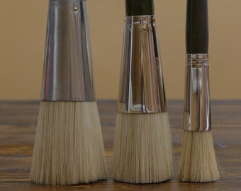 May include: Three paint brushes with black handles and silver ferrules. The brushes have natural bristles and are arranged in order of size from left to right.
